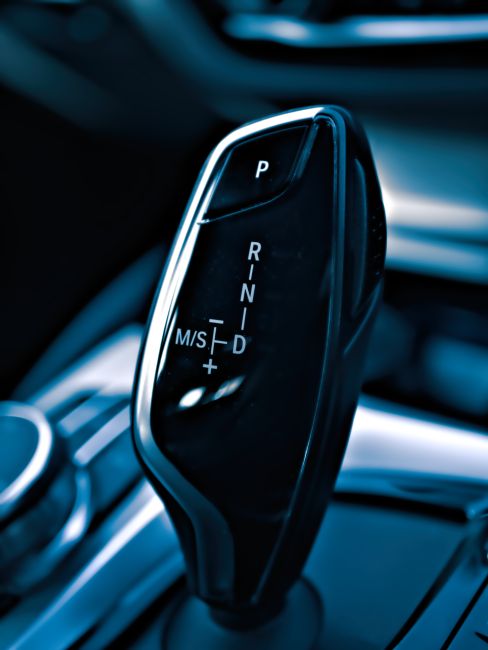 A close-up view of a modern, black automatic gear shift lever inside a car, with the gear options P, R, N, D, and M/S clearly visible, surrounded by sleek metallic and black interior trim, illuminated